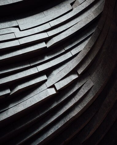 Close-up view of layered, curved, stone or concrete steps or panels, arranged in a pattern creating a sense of depth and texture.