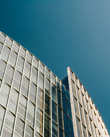 Modern glass office building with a curved facade against a clear blue sky.