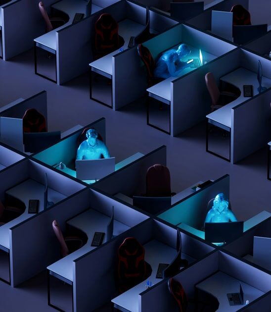 Rows of empty office cubicles with three people illuminated by the blue glow of their computer screens, working late in a darkened environment.