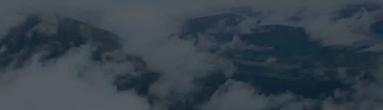 Clouds partially obscure a mountainous landscape, with peaks and ridges visible through gaps in the mist.