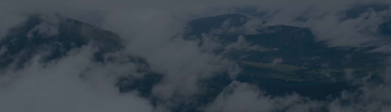 Clouds partially obscure a mountainous landscape, with peaks and ridges visible through gaps in the mist.