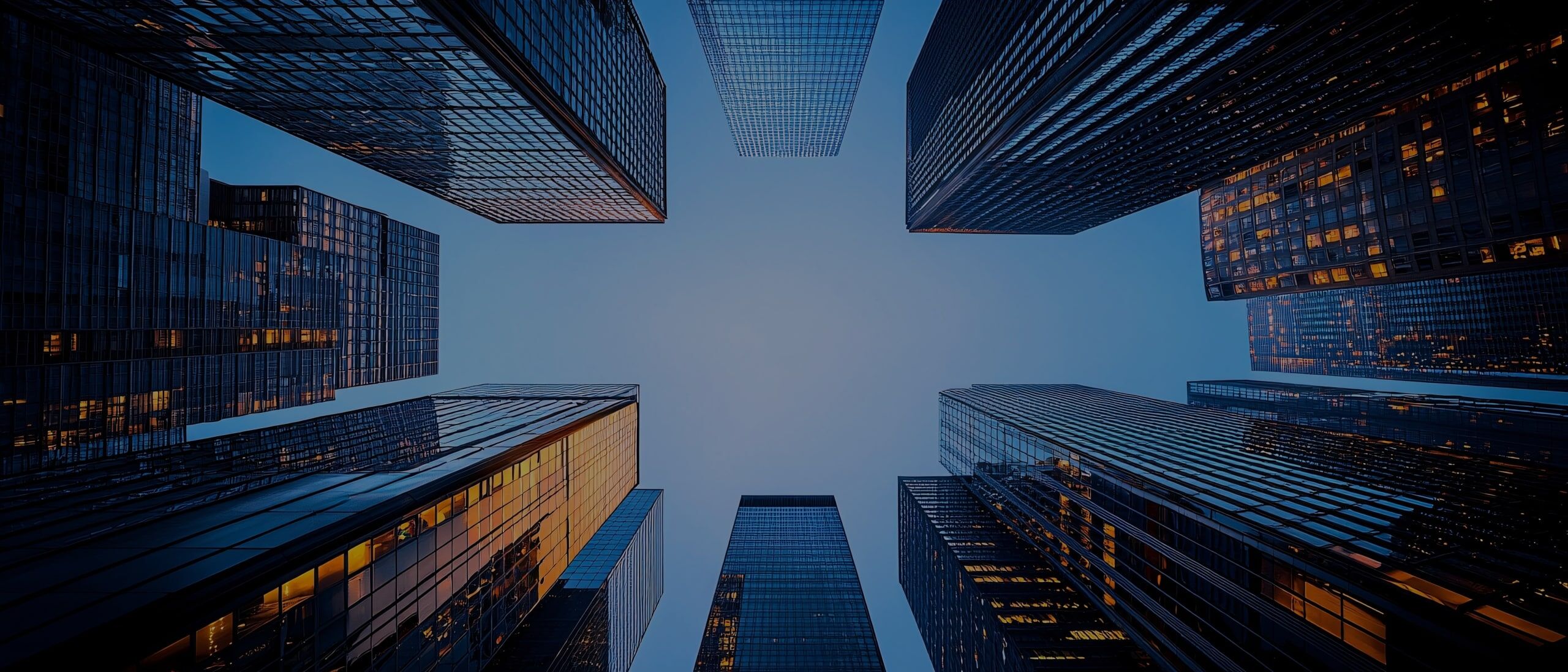 View looking up at tall modern skyscrapers with glass facades, forming a geometric pattern against a clear blue sky.
