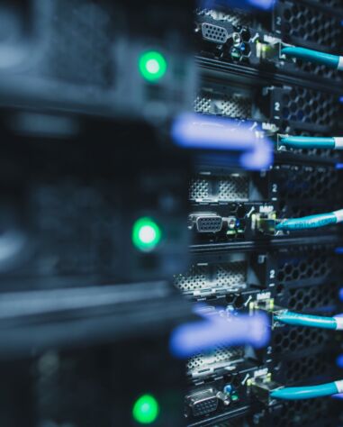Close-up of server racks with blue ethernet cables and green indicator lights in a data center.