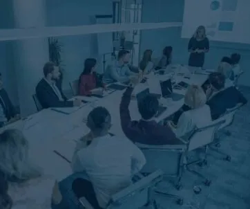 A group of people sit around a conference table watching a presenter give an ERP-focused presentation with charts projected on a screen.