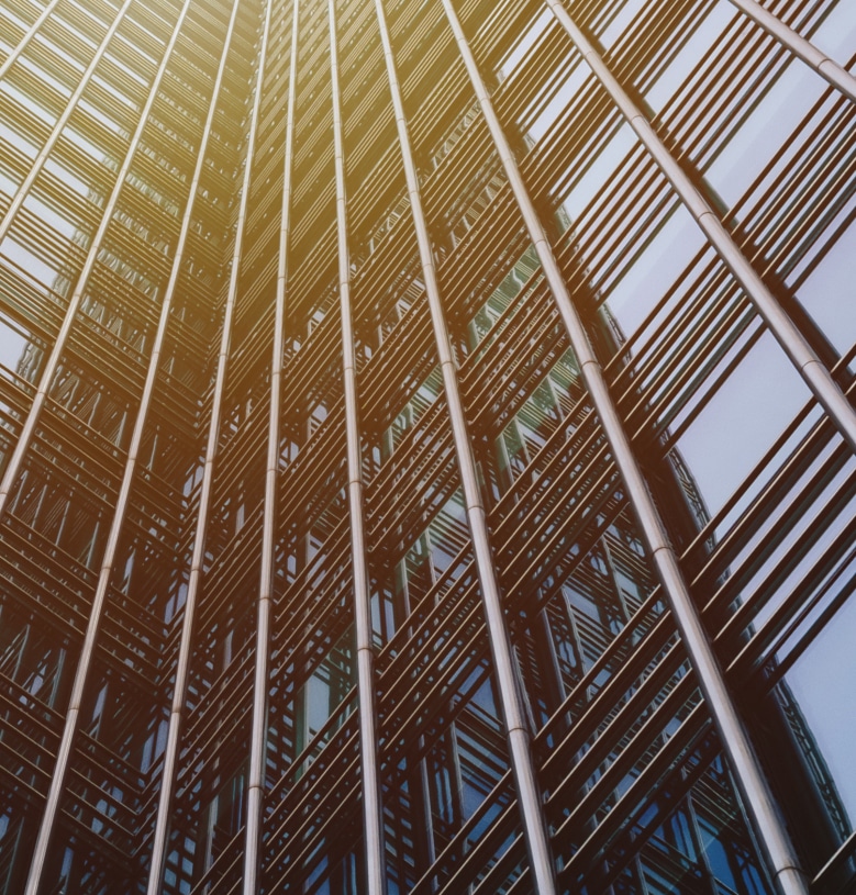 Close-up view of the exterior of a modern skyscraper with glass windows and metal framework, photographed from a low angle with sunlight reflecting off the building.