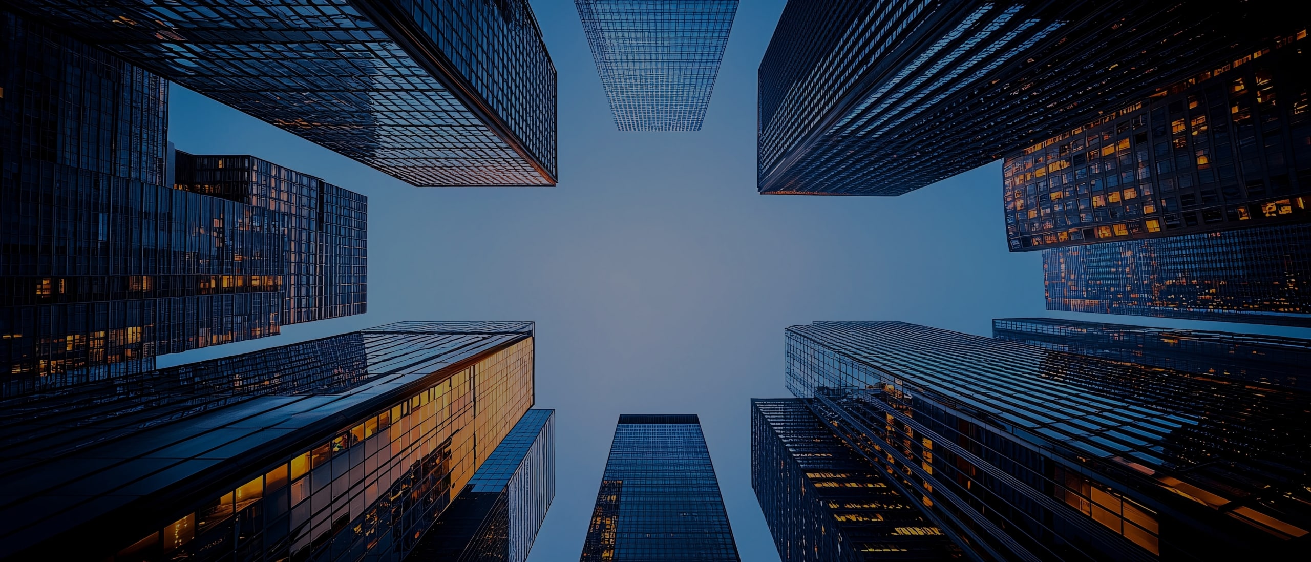 Skyscrapers viewed from below against a clear blue sky, with building lights reflecting off glass windows.