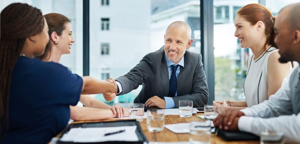 Business executives shaking hands at conference table during post-merger integration services meeting