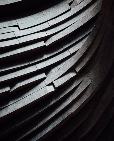 Close-up view of layered, curved, stone or concrete steps or panels, arranged in a pattern creating a sense of depth and texture.