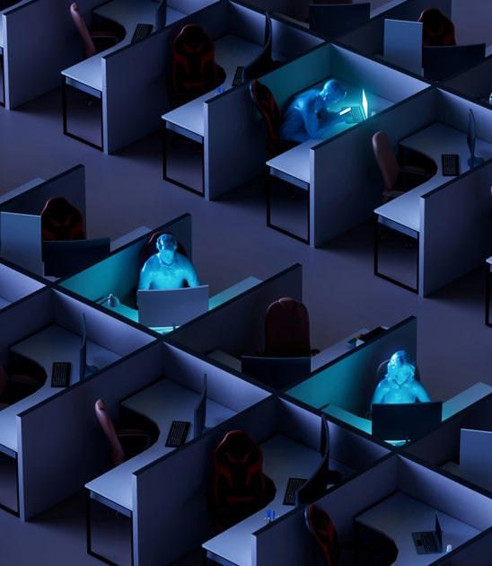 Rows of empty office cubicles with three people illuminated by the blue glow of their computer screens, working late in a darkened environment.