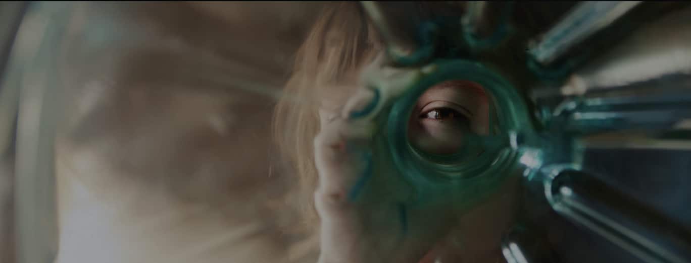 A person looks through a circular opening in a translucent, greenish object, with only one eye and part of their face visible.