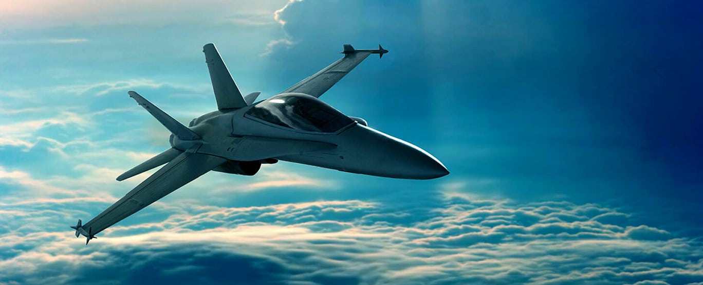 A fighter jet flies above the clouds in a clear blue sky, illuminated by sunlight from the upper right.