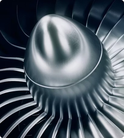 Close-up view of a shiny metallic jet engine turbine fan with sleek, curved blades arranged in a circular pattern.