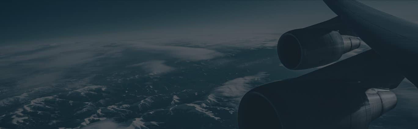 View from an airplane window showing the aircraft's engine and wing above a landscape of mountains and clouds.