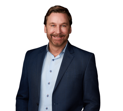 Man in a blue suit jacket and light blue button-up shirt smiling, standing against a plain white background.
