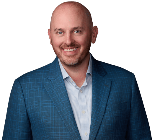 A bald man with a short beard is smiling, wearing a blue checkered suit jacket and a light-colored shirt, posed against a plain white background.