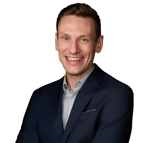 A man in a dark suit and light dress shirt smiles with arms crossed against a plain white background.
