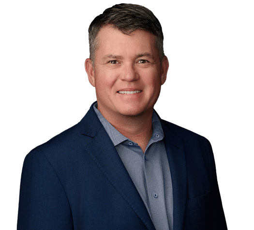 Man wearing a blue suit jacket and light blue shirt, smiling, against a plain light background.