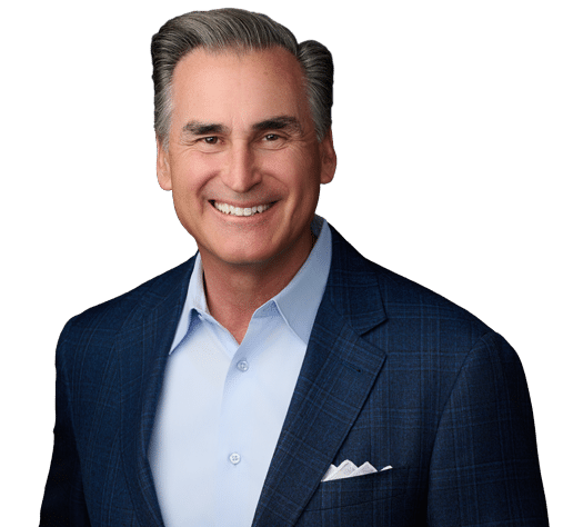 Smiling man with gray hair wearing a blue blazer, light blue dress shirt, and white pocket square against a plain background.