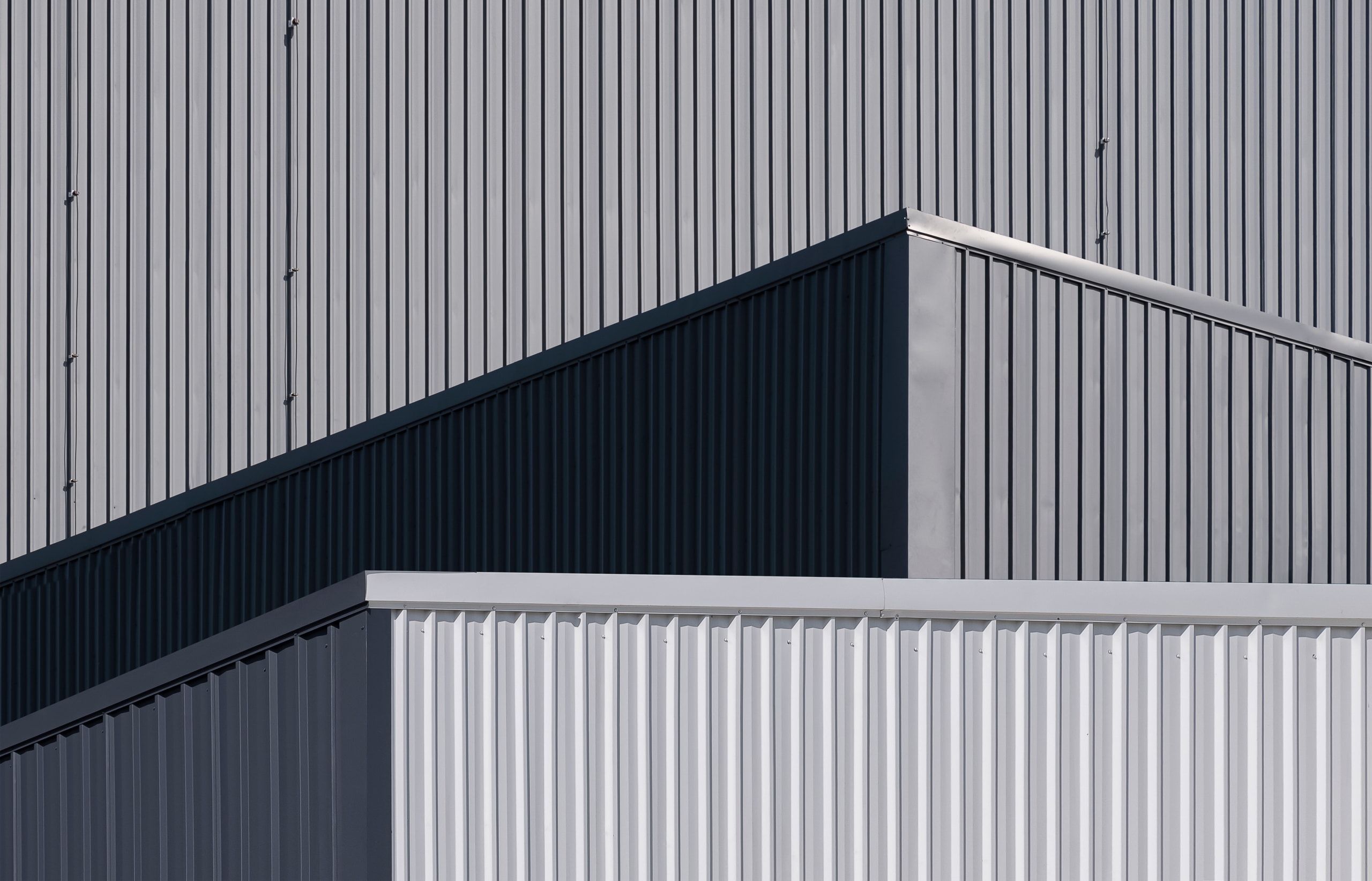 Close-up view of an industrial building with overlapping metal wall panels and geometric lines in shades of gray and white.