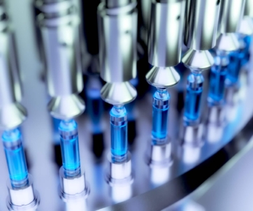 Close-up of an automated assembly line filling glass vials with blue liquid, likely for pharmaceutical or laboratory use.