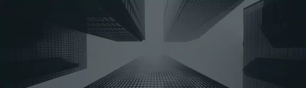 View looking up at tall, modern skyscrapers with glass facades against a cloudy or foggy sky.