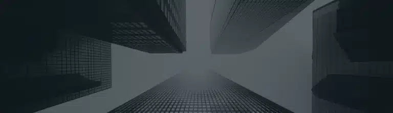 View looking up at tall, modern skyscrapers with glass facades against a cloudy or foggy sky.