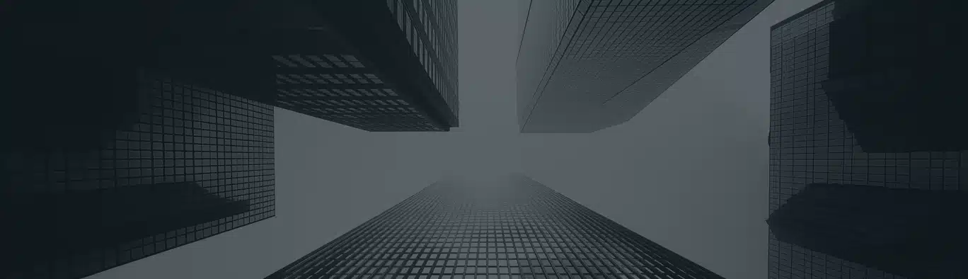 View looking up at tall, modern skyscrapers with glass facades against a cloudy or foggy sky.