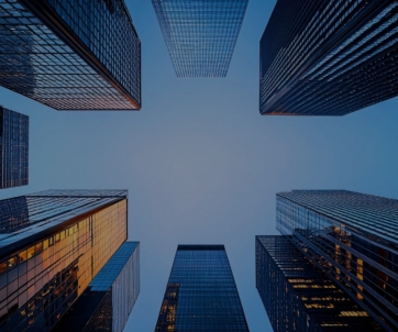 View looking up at tall modern skyscrapers with glass facades, forming a geometric pattern against a clear blue sky.