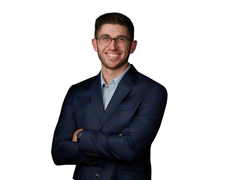 A man wearing glasses and a navy blazer stands with arms crossed, smiling, against a plain white background.