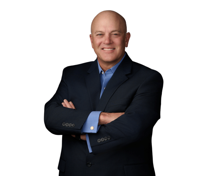 Bald man in a dark suit with a blue shirt, standing with arms crossed and smiling against a plain white background.