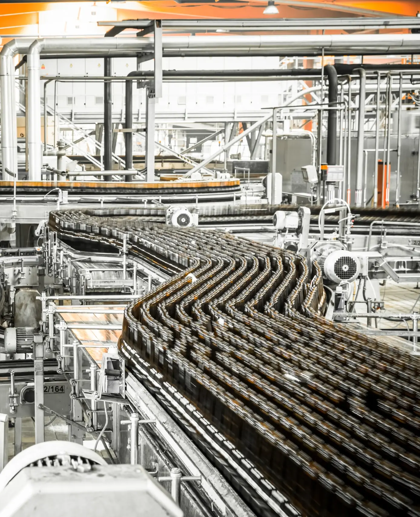 Bottles move along winding conveyor belts in a modern factory, surrounded by metal pipes, machinery, and industrial equipment.