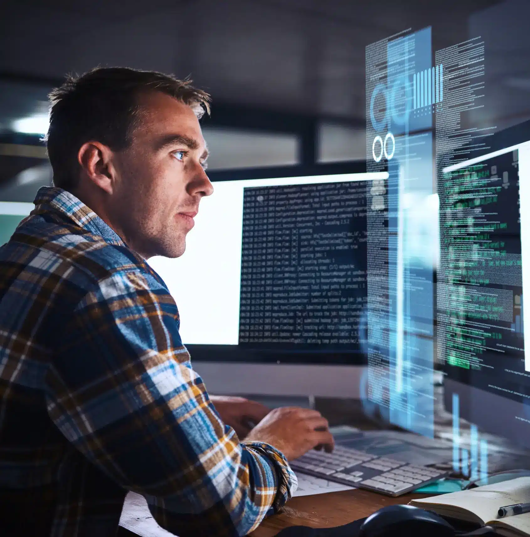 Man in plaid shirt sits at a desk with multiple monitors, typing code on a keyboard, with holographic data and code visualizations projected in front of him.