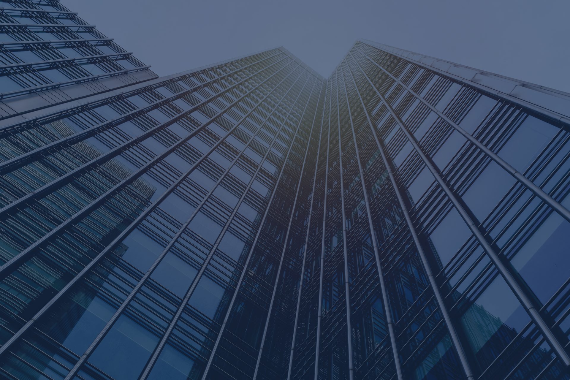 Upward view of a modern glass skyscraper with reflective windows, converging towards the sky, creating strong diagonal lines and a symmetrical perspective.