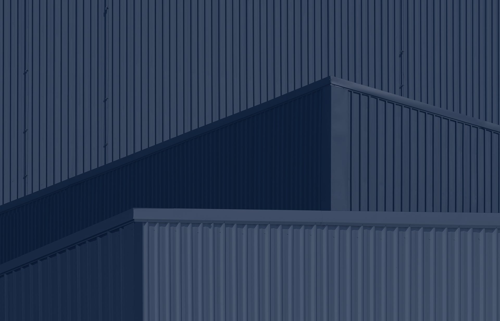 Close-up of a modern industrial building exterior featuring geometric shapes and vertical metal siding in a monochromatic blue color palette.