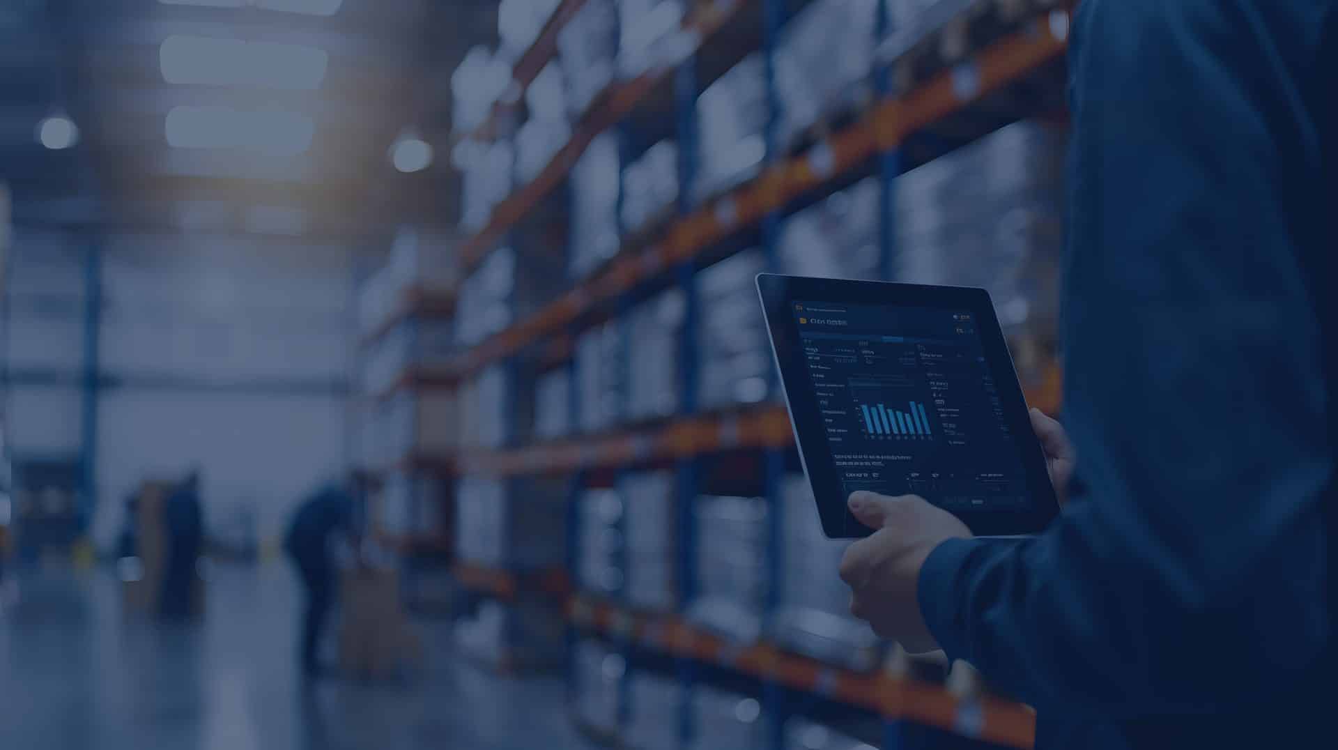 Person holding a tablet displaying data in a warehouse with shelves of boxes and two workers in the background.