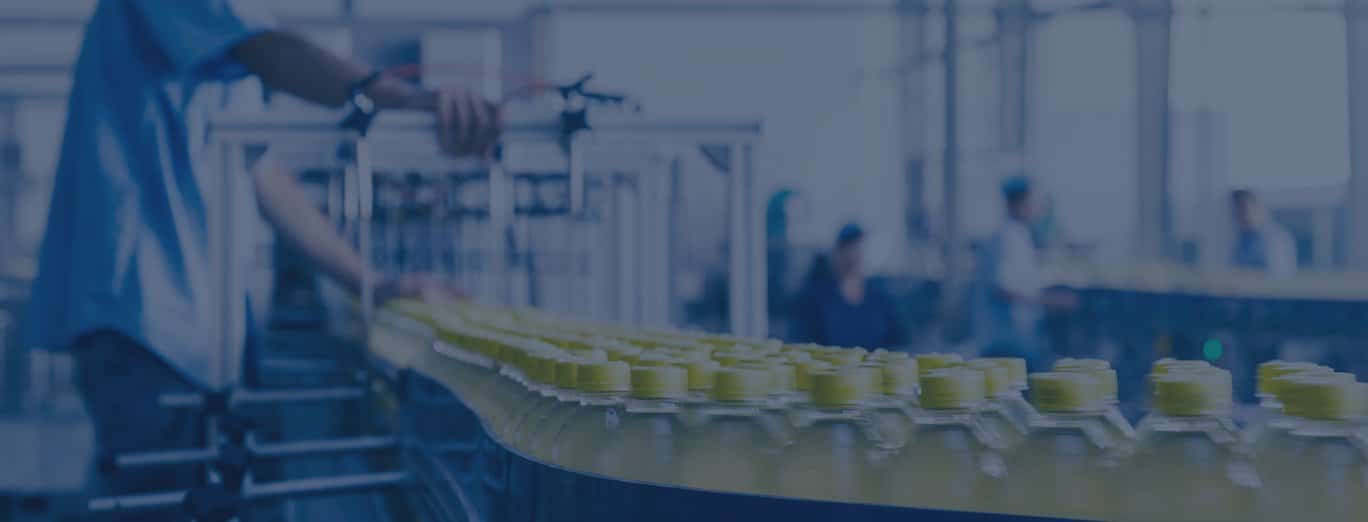 A conveyor belt moves rows of yellow-capped bottles through a factory, where workers in the background operate machinery as part of a facility that prioritizes food safety consulting standards.