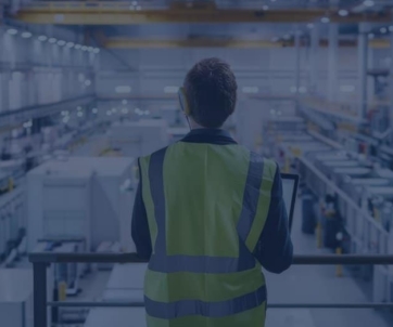 Person in a high-visibility vest stands on a platform overlooking large industrial machinery and equipment inside a factory, embodying the principles of operations improvement consulting.
